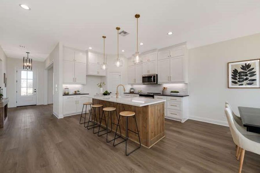 Kitchen with white cabinetry, an island with sink, brown cabinets, a breakfast bar, and stainless steel microwave Kitchen with white cabinetry, an island with sink, brown cabinets, a breakfast bar, and stainless steel microwave