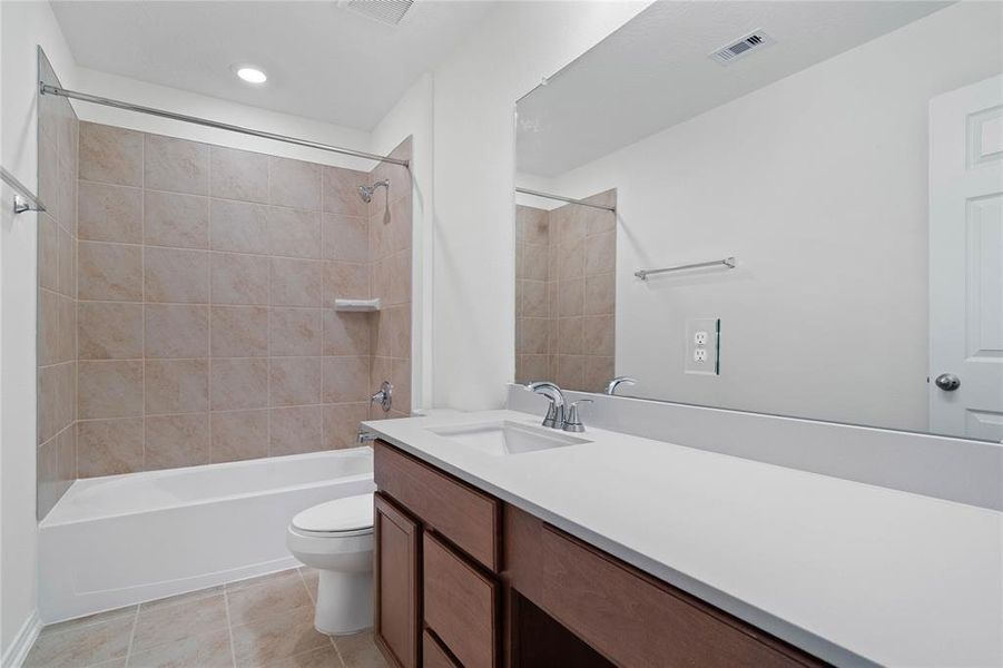 Secondary bath features tile flooring, tub/shower combo with tile surround, stained wood cabinets, beautiful light countertops, mirror, sleek fixtures and modern finishes.