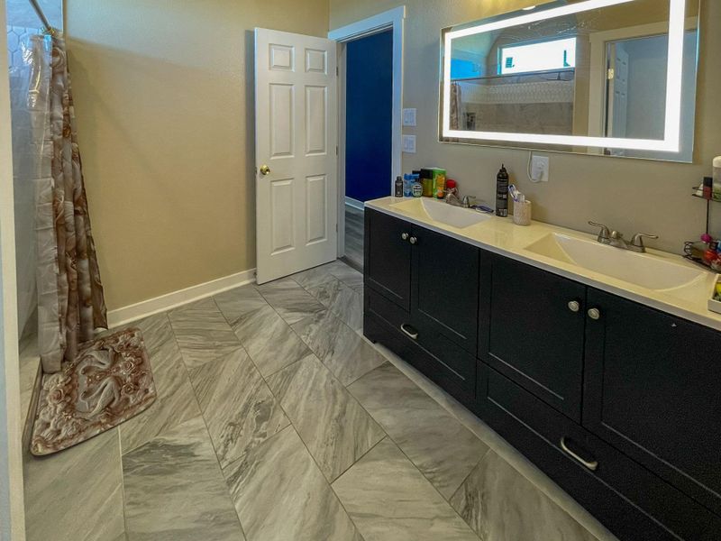 Bathroom featuring double vanity, curtained shower, and light marble finish floors