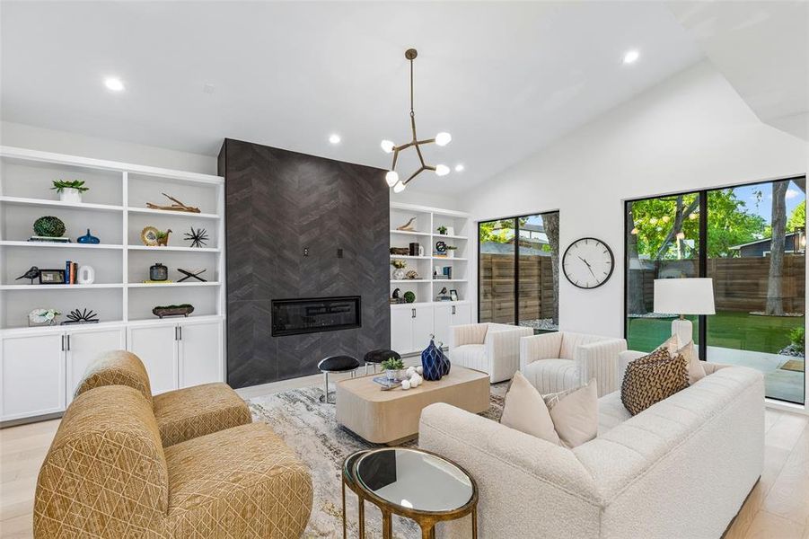 Light-filled living room with vaulted ceilings, custom built-ins, and a striking fireplace, seamlessly connected to the backyard through expansive windows.