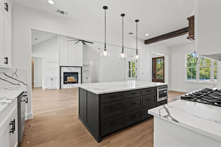 Kitchen with light stone counters, pendant lighting, a kitchen island, white cabinetry, and recessed lighting Kitchen with light stone counters, pendant lighting, a kitchen island, white cabinetry, and recessed lighting