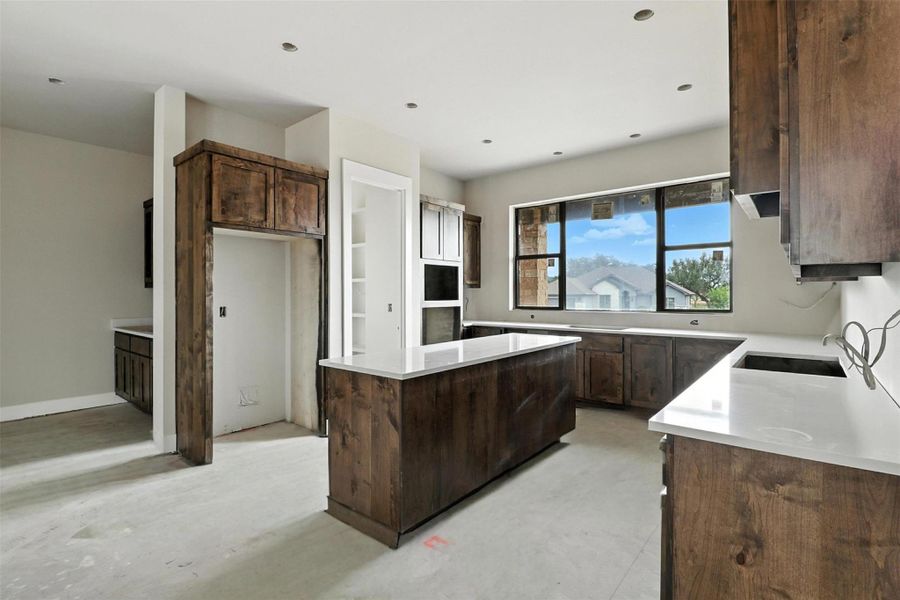 Kitchen featuring dark brown cabinets, a kitchen island, concrete flooring, light stone countertops, and recessed lighting Kitchen featuring dark brown cabinets, a kitchen island, concrete flooring, light stone countertops, and recessed lighting