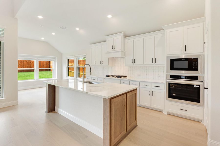 Kitchen with white cabinets, large island, quartz countertops, and stainless steel built-in oven and microwave Kitchen with white cabinets, large island, quartz countertops, and stainless steel built-in oven and microwave