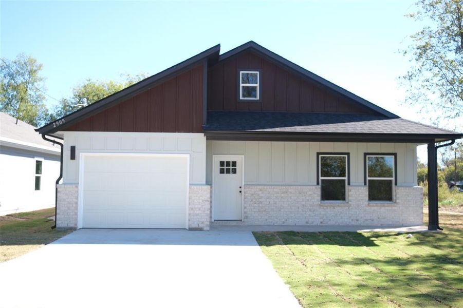 View of front of property with board and batten siding, brick siding, a front lawn, a porch, and concrete driveway View of front of property with board and batten siding, brick siding, a front lawn, a porch, and concrete driveway