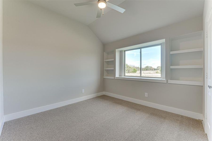 Carpeted spare room with lofted ceiling, ceiling fan, and built in features