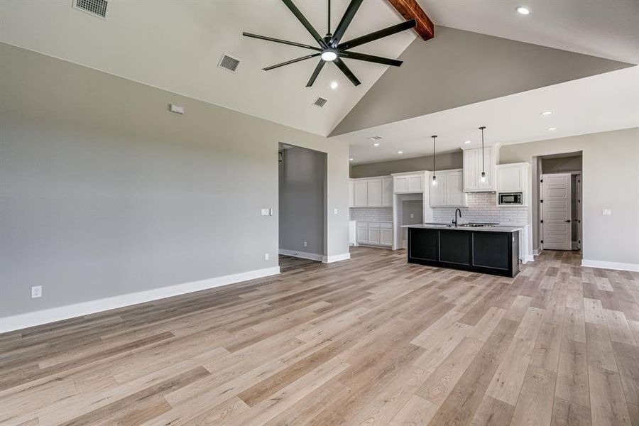 Unfurnished living room featuring beam ceiling, ceiling fan, light hardwood / wood-style flooring, and high vaulted ceiling