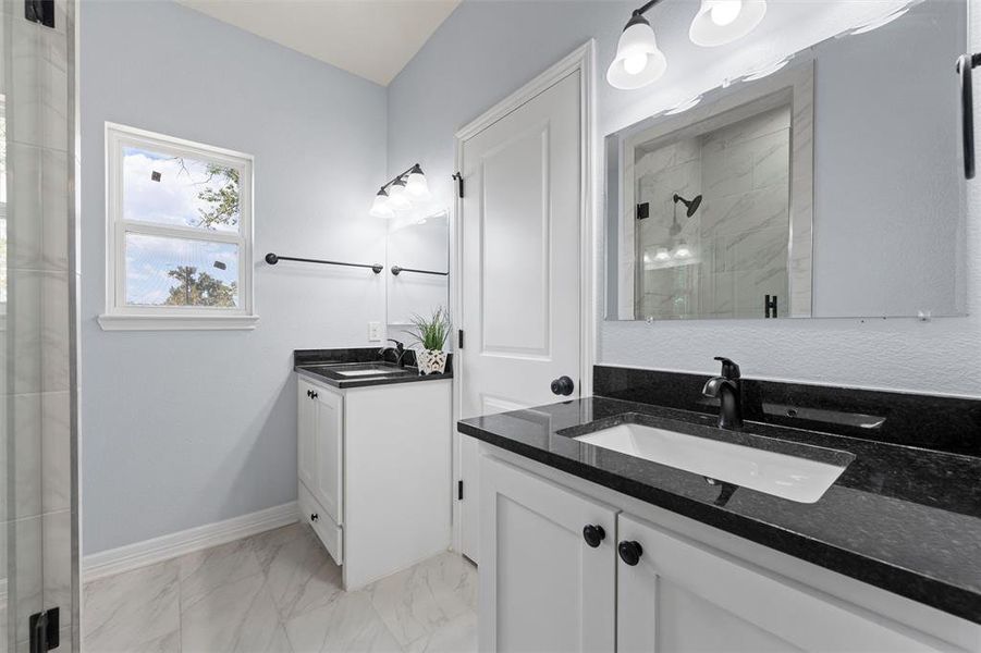 Full bathroom featuring a shower stall, two vanities, and light marble finish floors