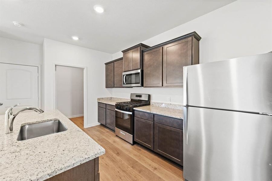 Kitchen featuring light stone counters, appliances with stainless steel finishes, dark cabinets, sink, and light wood-style floors