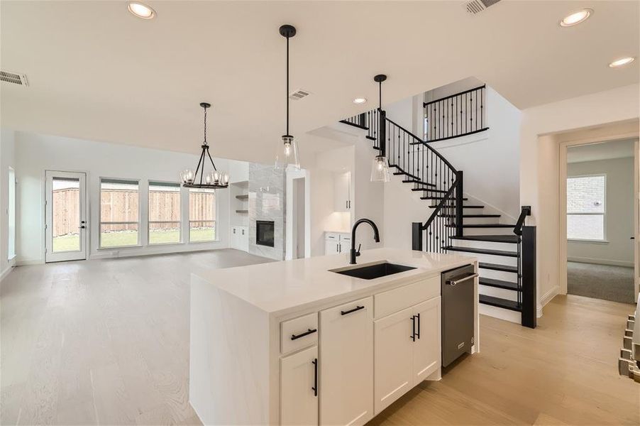 Kitchen featuring white cabinets, hanging light fixtures, a center island with sink, light wood-type flooring, and sink