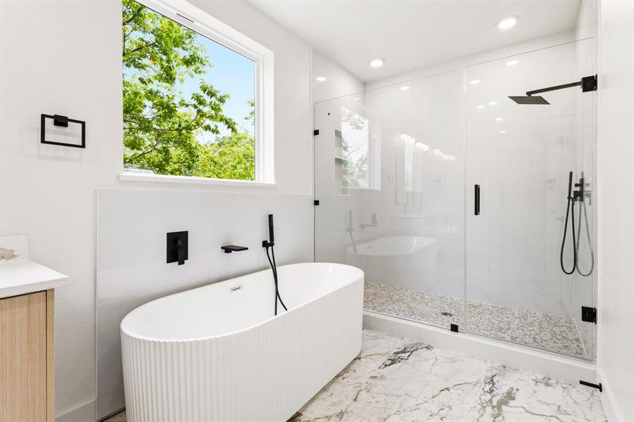 The bathroom features a freestanding tub, a glass-enclosed shower with a rainfall showerhead, and a window providing natural light