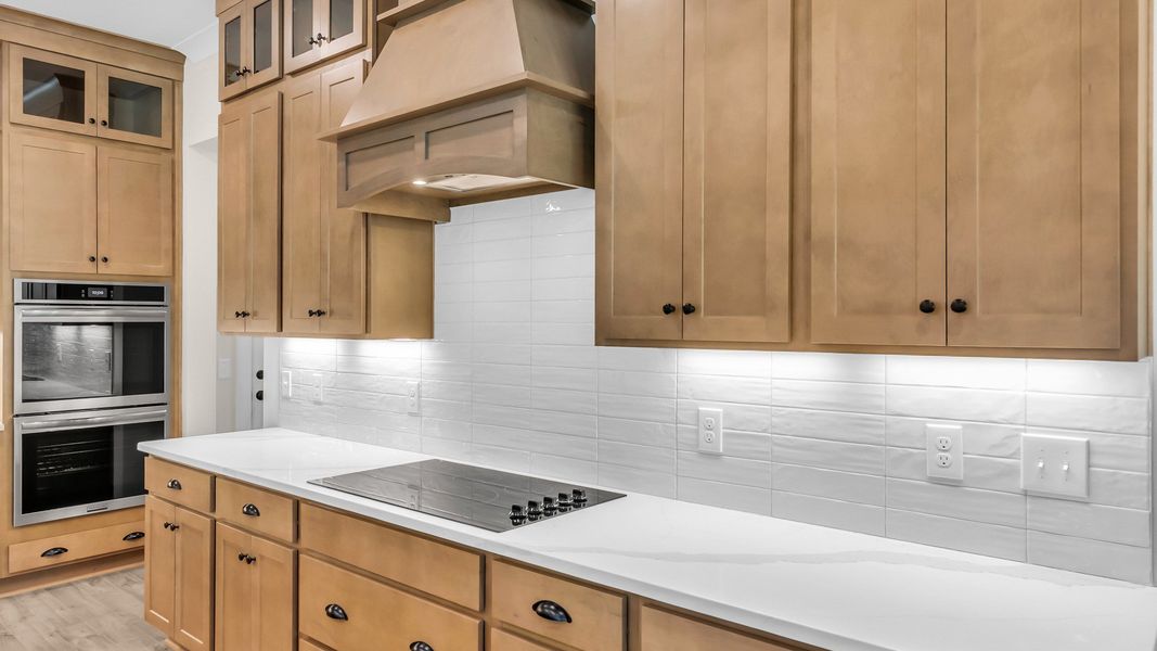 Kitchen with wood colored cabinetry and nearby gathering room (Representative of completed home)