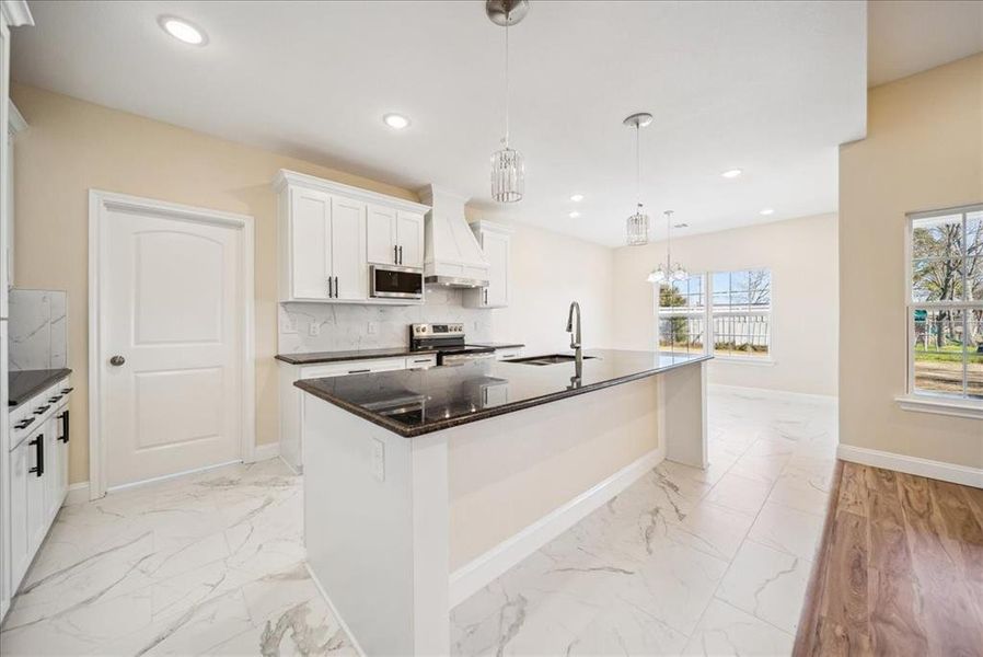 Kitchen featuring custom exhaust hood, sink, an island with sink, appliances with stainless steel finishes, and white cabinetry