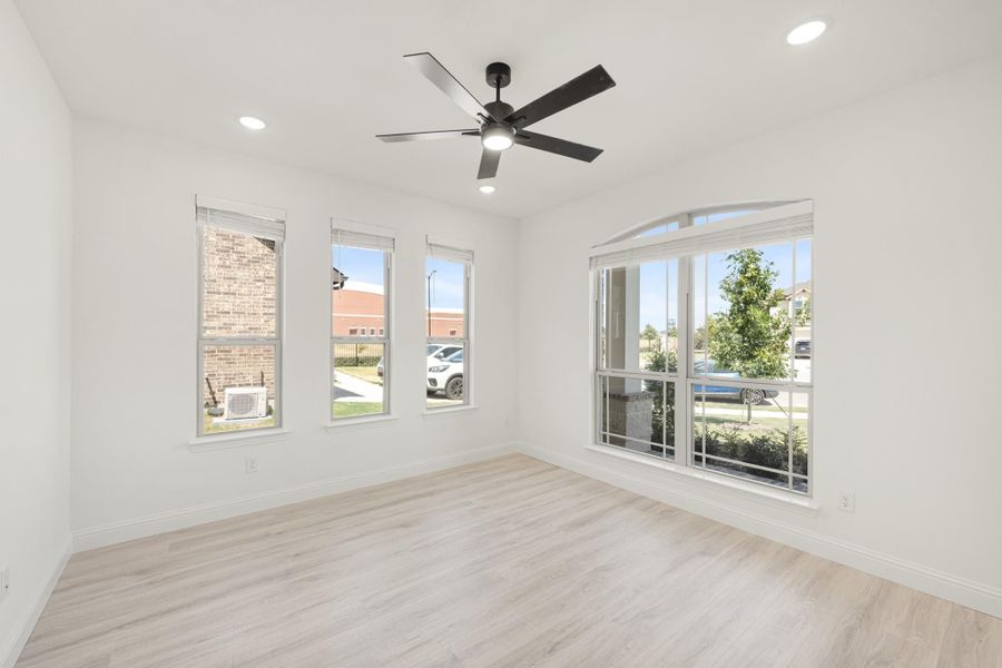 Empty room with light wood floors, white walls, ceiling fan, and large windows with neighborhood views