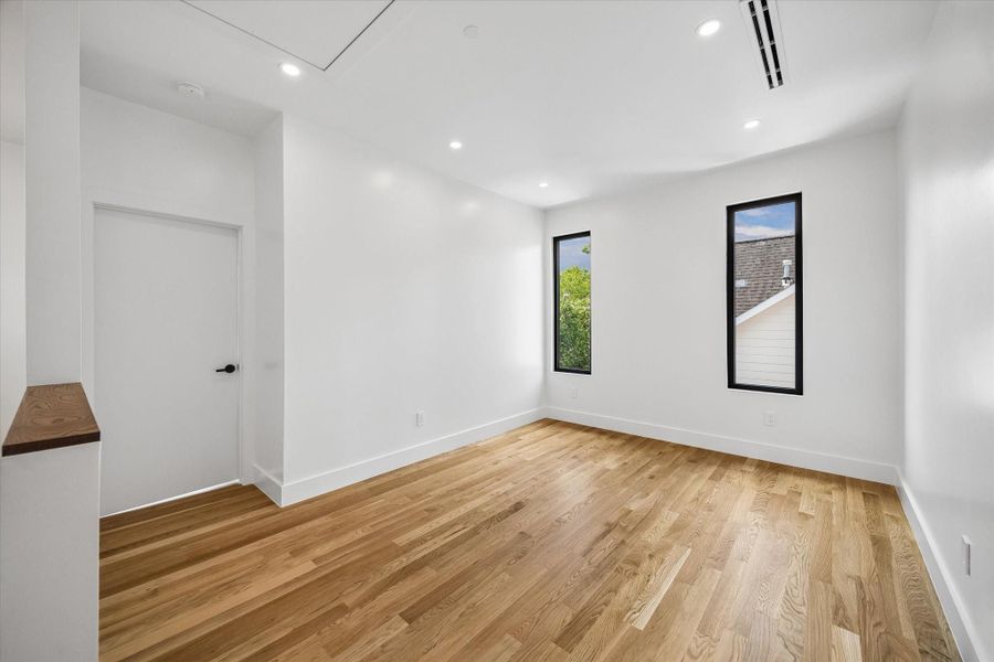 Bright and inviting room featuring hardwood floors, fresh white walls, and two tall windows offering ample natural light. Bright and inviting room featuring hardwood floors, fresh white walls, and two tall windows offering ample natural light.