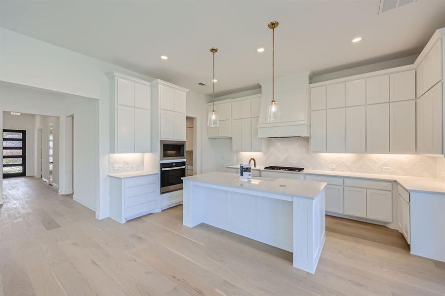 Kitchen featuring an island with sink, appliances with stainless steel finishes, light hardwood / wood-style floors, and white cabinetry