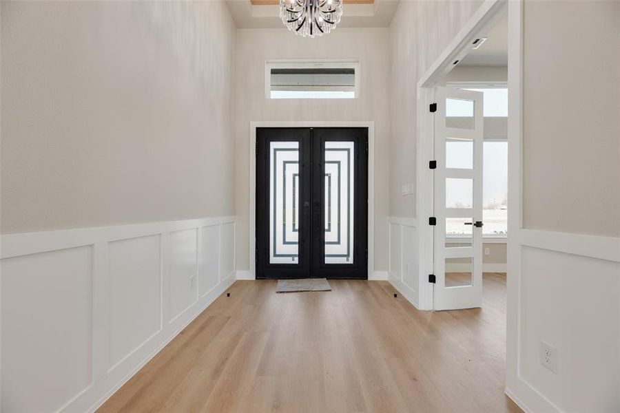 Entryway with a decorative wall, french doors, hanging lights, a wainscoted wall, and light wood-style floors