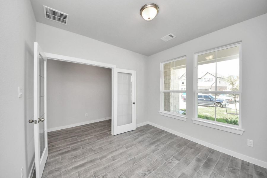 Experience the perfect blend of sophistication and warmth in this home office, boasting elegant wood-look tile flooring and flooded with natural light from expansive windows and French doors. Sample photo of completed home with similar floor plan. Actual colors and selections may vary.
