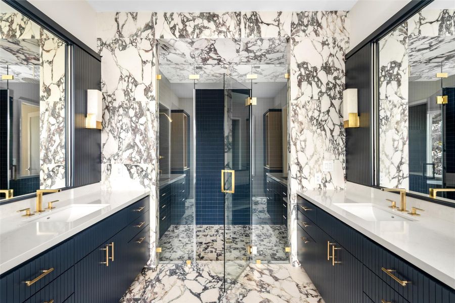 An elevated primary bath anchored by dual vanities & bold surfaces, paired with fluted navy cabinetry and layered brass details for a polished look.