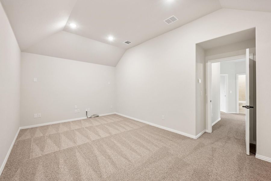 Empty bedroom with vaulted ceiling, beige carpet, and white walls leading to hallway