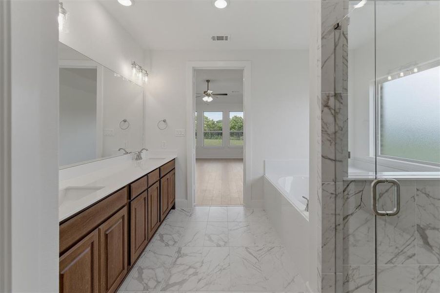 Spacious bathroom featuring a dual vanity with wood cabinetry and white countertops, a large frameless glass shower enclosure, a built-in soaking tub, and marble-look tile flooring Spacious bathroom featuring a dual vanity with wood cabinetry and white countertops, a large frameless glass shower enclosure, a built-in soaking tub, and marble-look tile flooring