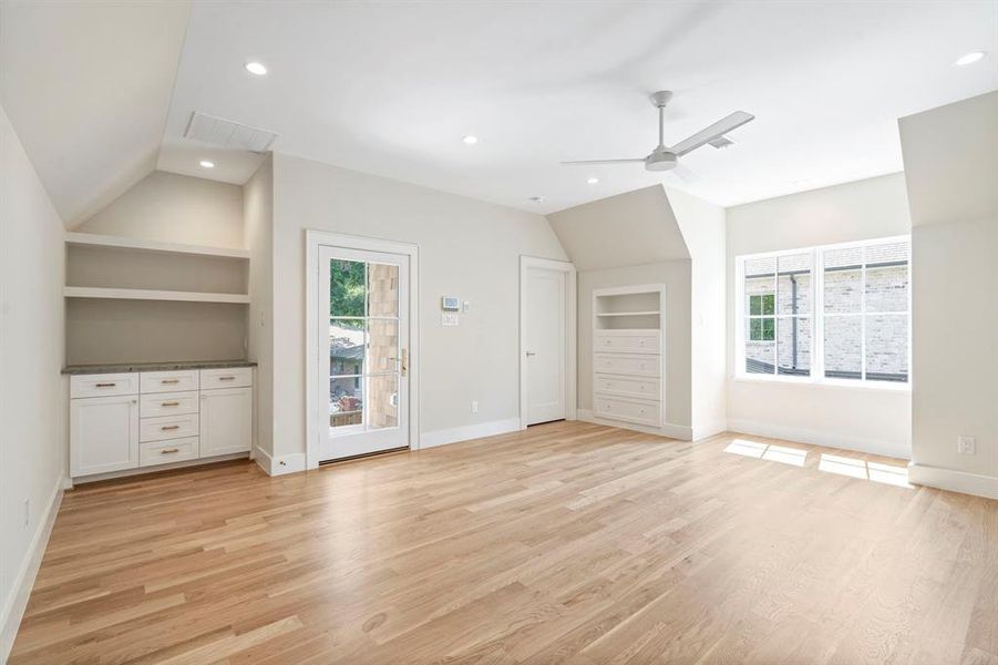 Unfurnished living room featuring built in shelves, vaulted ceiling, ceiling fan, and light wood-type flooring