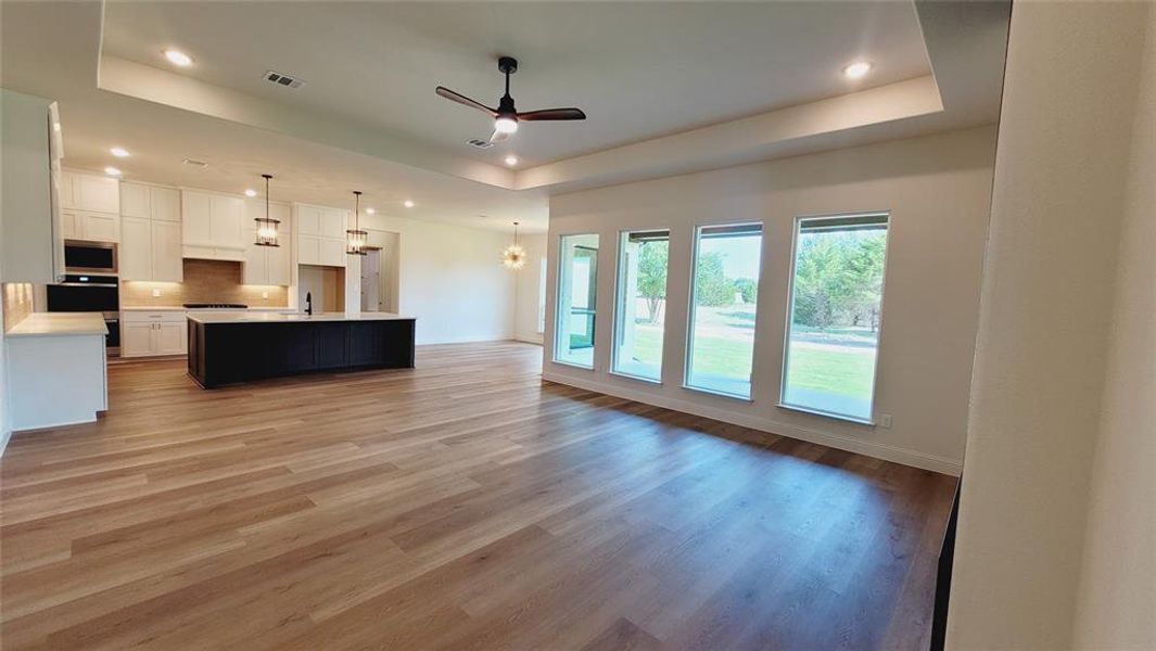 Spacious open-concept interior featuring light wood-finish flooring, recessed lighting, a modern ceiling fan, and a kitchen with an island, pendant lighting, and white cabinetry