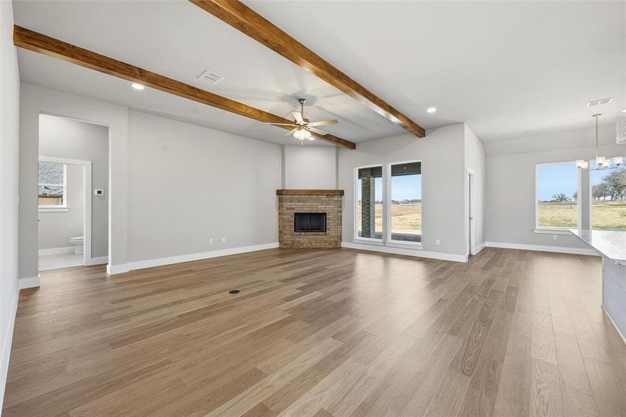 Unfurnished living room with a fireplace, light wood-type flooring, healthy amount of natural light, ceiling fan, and beam ceiling