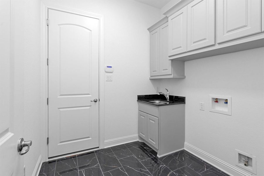 The laundry room is both functional and refined, offering upper cabinetry, a utility sink, and polished black granite counters atop striking marble tile floors. The laundry room is both functional and refined, offering upper cabinetry, a utility sink, and polished black granite counters atop striking marble tile floors.