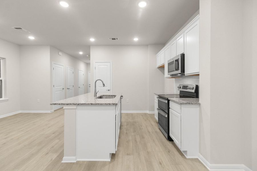 The kitchen features white cabinetry, stainless steel appliances, and a central island with a sink and granite countertops