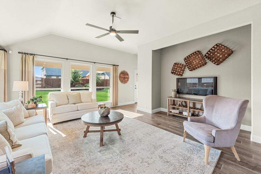 Living room with vaulted ceiling, ceiling fan, hardwood floors, and large windows overlooking backyard