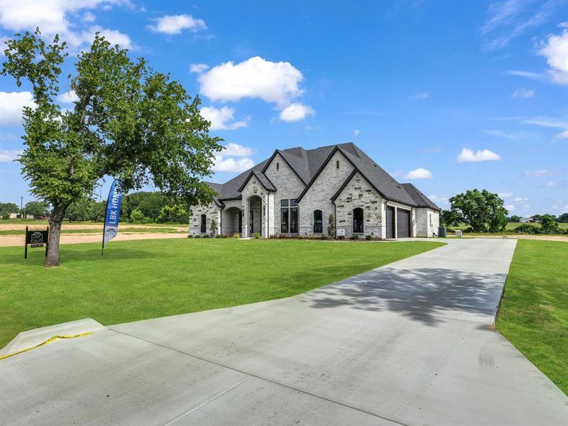 French country home featuring an attached garage, concrete driveway, and a front yard French country home featuring an attached garage, concrete driveway, and a front yard
