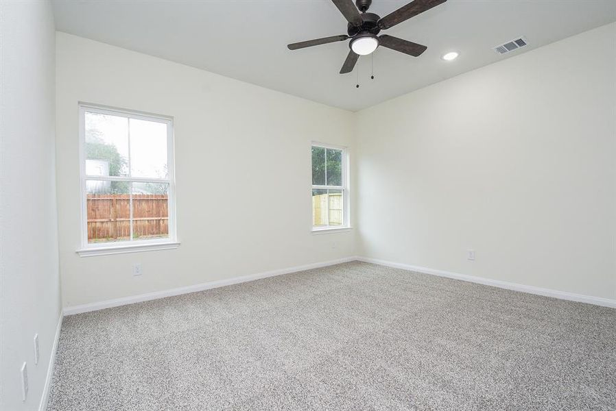 Gameroom with beige walls, a textured carpet, two windows, and a ceiling fan.