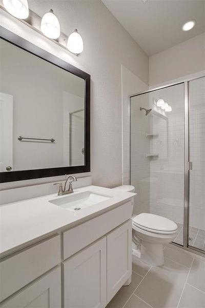 Bathroom with vanity, toilet, a shower with shower door, and tile patterned floors