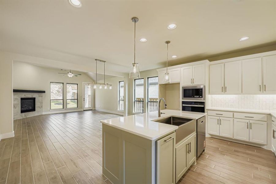 Kitchen with tasteful backsplash, a kitchen island with sink, open floor plan, light wood finished floors, and pendant lighting