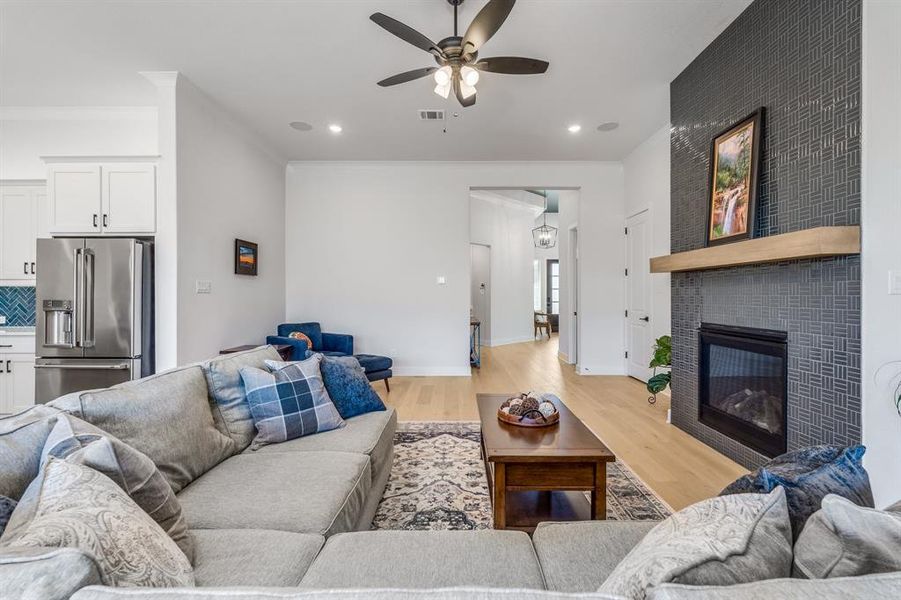 Living room with a tiled fireplace, ceiling fan, crown molding, and light hardwood / wood-style floors