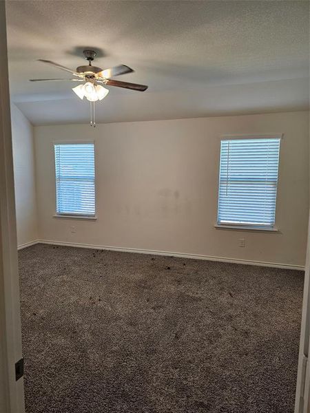 Empty room with a textured ceiling, dark carpet, and ceiling fan