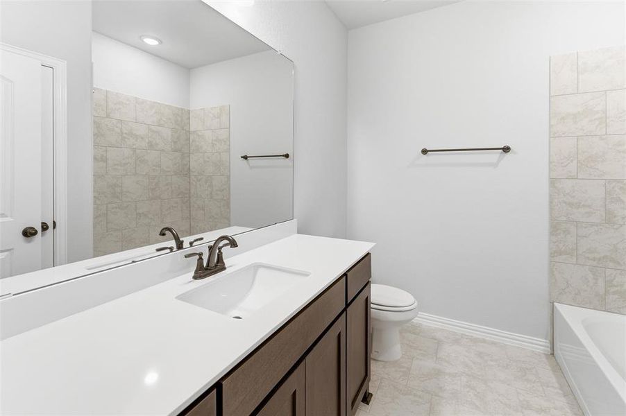 Bathroom featuring a white integrated sink with bronze-finish faucet, dark wood-finish cabinetry, and a large frameless mirror