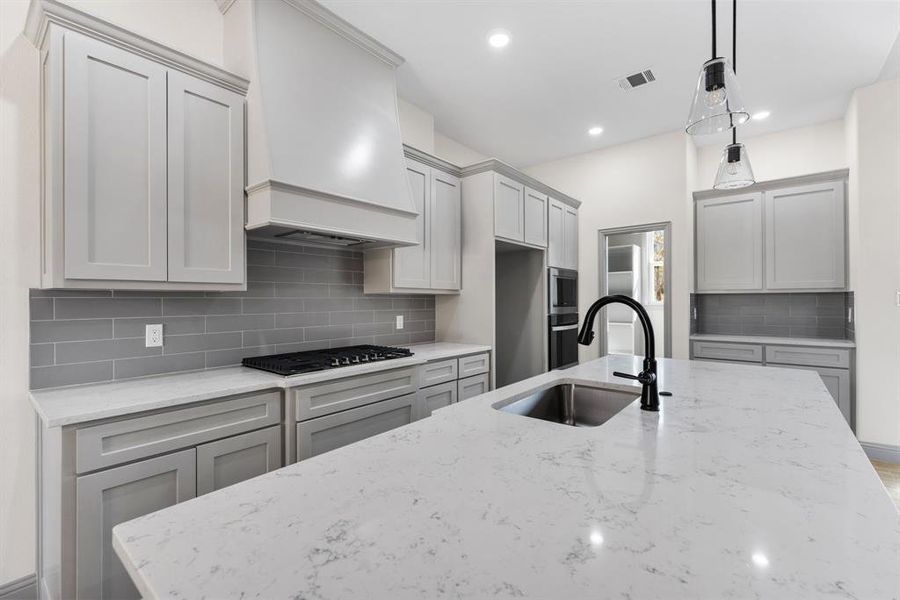 Kitchen featuring tasteful backsplash, gray cabinetry, light stone counters, decorative light fixtures, and recessed lighting