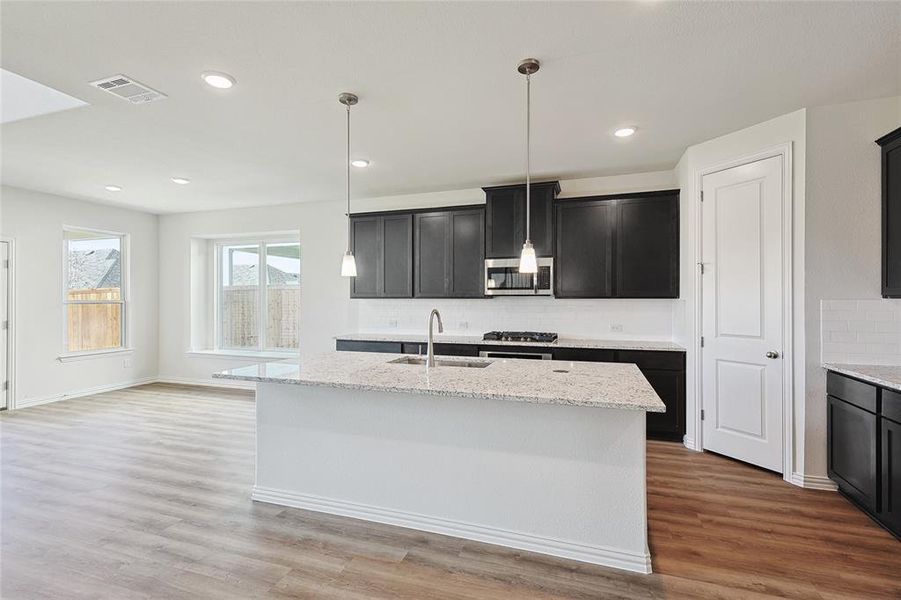 Kitchen featuring light stone countertops, light hardwood / wood-style flooring, appliances with stainless steel finishes, an island with sink, and sink