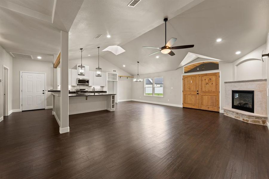 Unfurnished living room featuring a ceiling fan, a stone fireplace, dark wood-style flooring, a sink, and baseboards