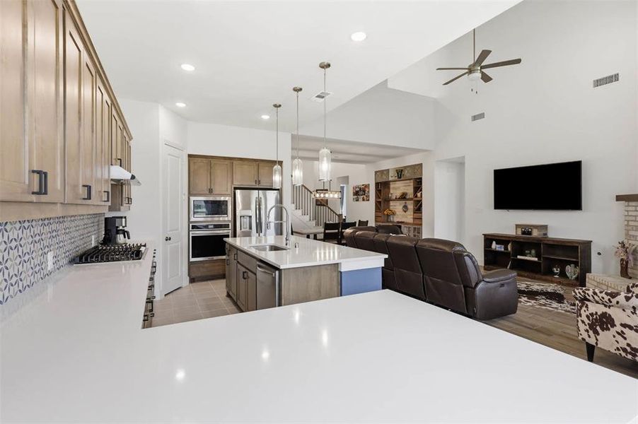 Open-concept kitchen and living area featuring light wood-finish cabinetry, white countertops, stainless steel appliances, and a gas range