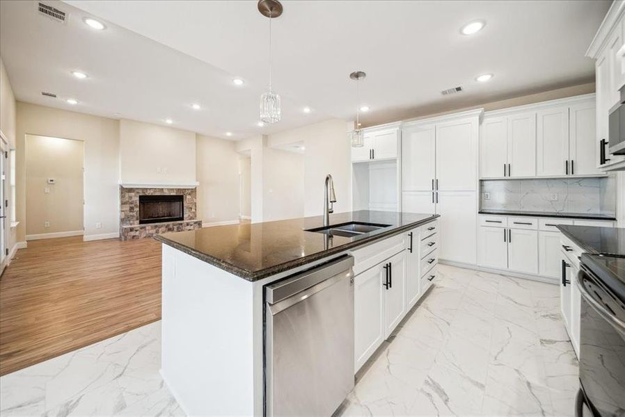 Kitchen featuring a kitchen island with sink, white cabinets, hanging light fixtures, sink, and stainless steel dishwasher