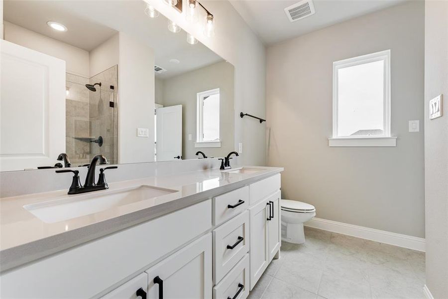 Bathroom featuring tiled shower, vanity, toilet, and tile patterned flooring