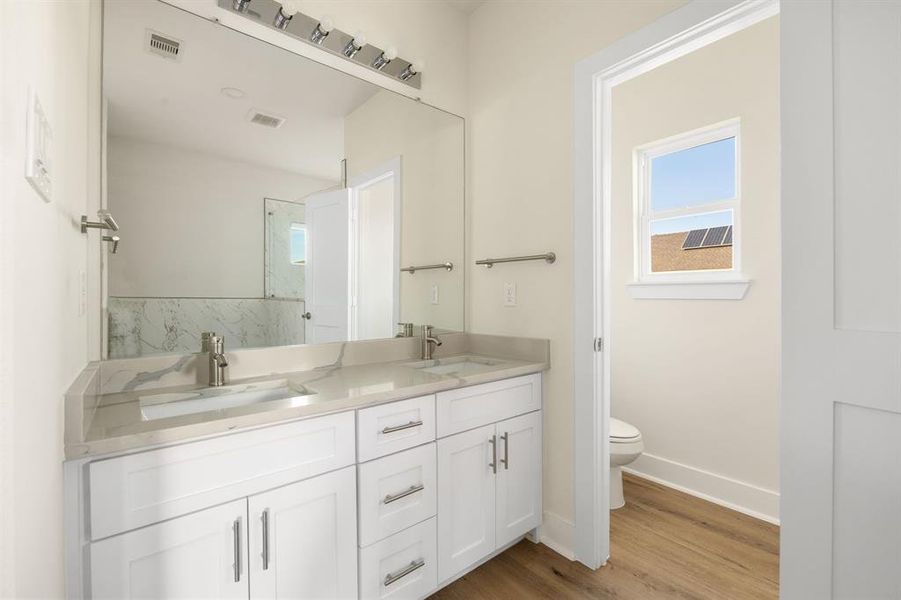 Primary bath features a modern vanity with granite countertops, a sleek sink, and a large framed mirror for a sophisticated, polished look.