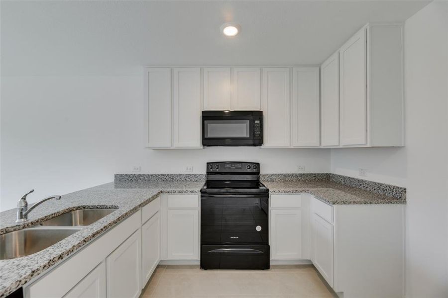 Kitchen with black appliances, white cabinets, sink, light stone countertops, and light tile patterned flooring