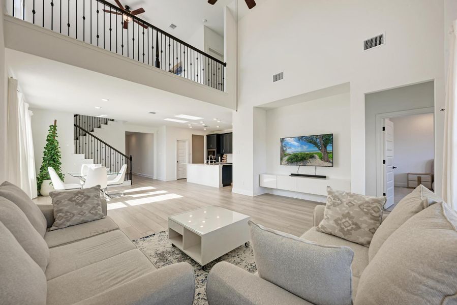 Living area featuring light wood-style floors, ceiling fan, stairway, and a high ceiling