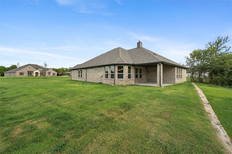 Rear view of property with a lawn, a chimney, a patio, and brick siding