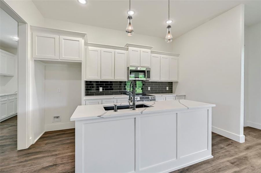 Kitchen with decorative backsplash, a sink, white cabinets, stainless steel microwave, and an island with sink