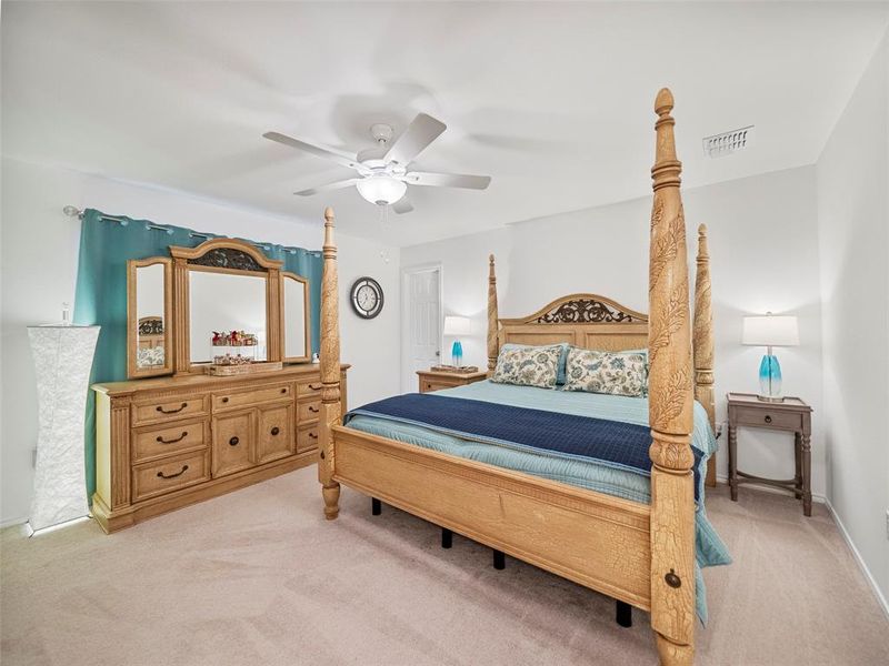 Bedroom featuring a ceiling fan, visible vents, and light carpet