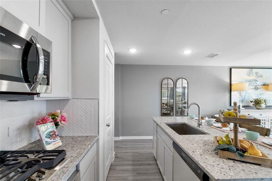 Kitchen featuring hardwood / wood-style floors, sink, light stone countertops, decorative backsplash, and appliances with stainless steel finishes